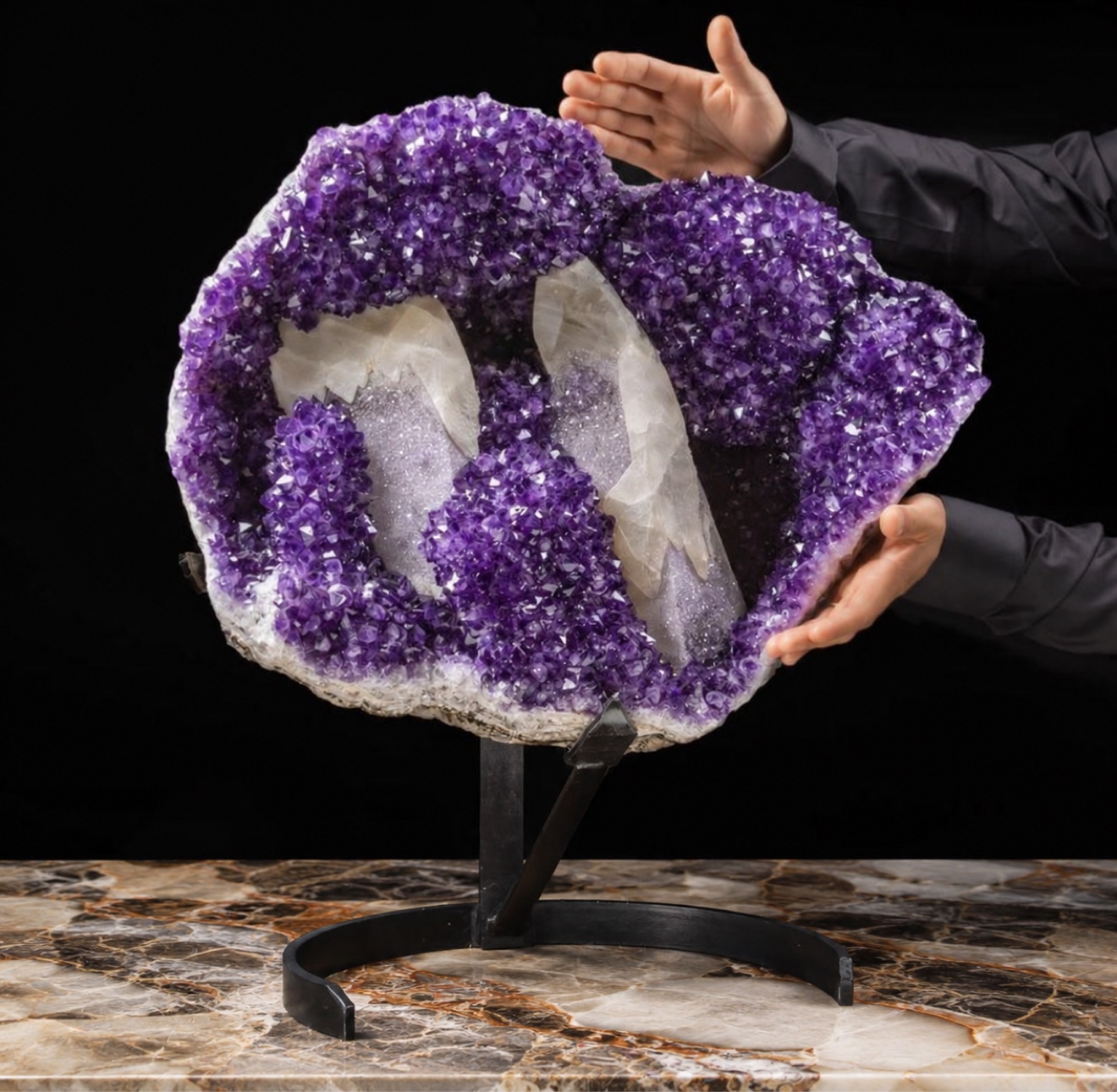 Monumental amethyst geode ring sculpture on a black stand, presented by hand against black