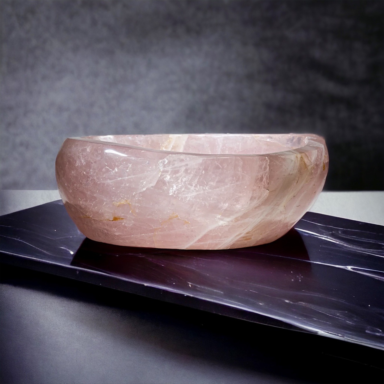 Polished rose quartz bowl with soft blush veining on dark marble