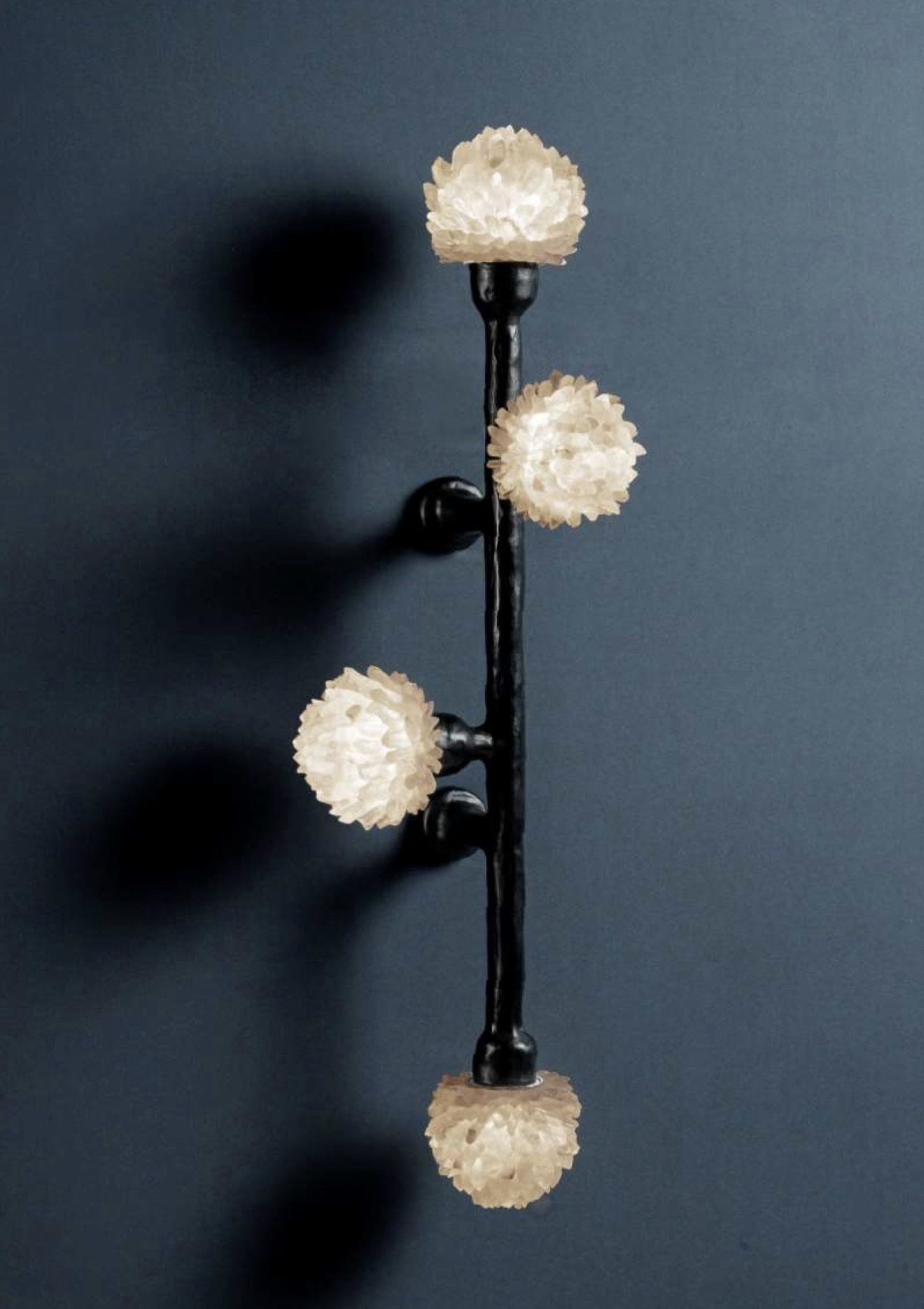Black sculptural wall light with four glowing crystal cluster globes on a deep slate wall