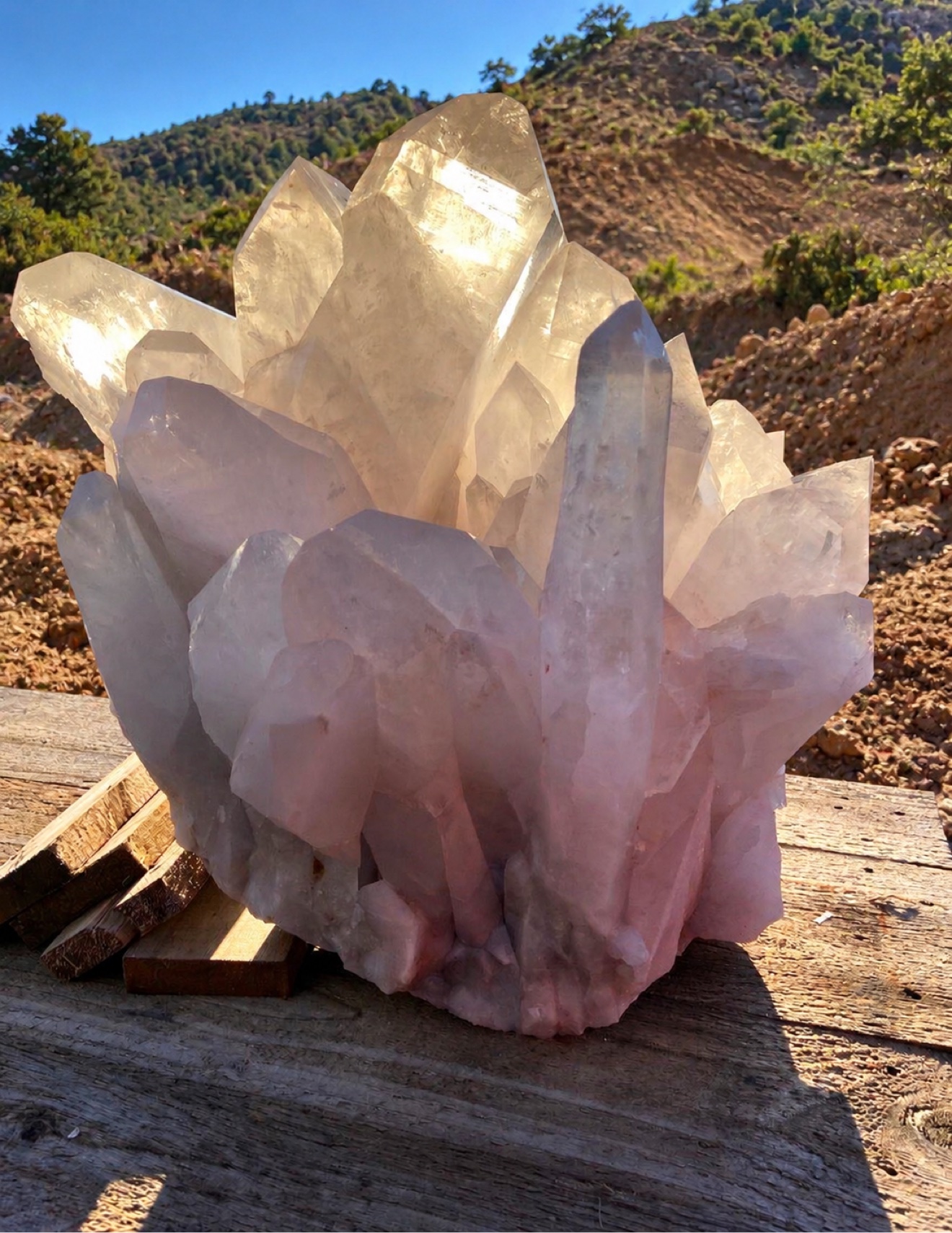 Monumental clear quartz cluster at the mine, mountain landscape behind