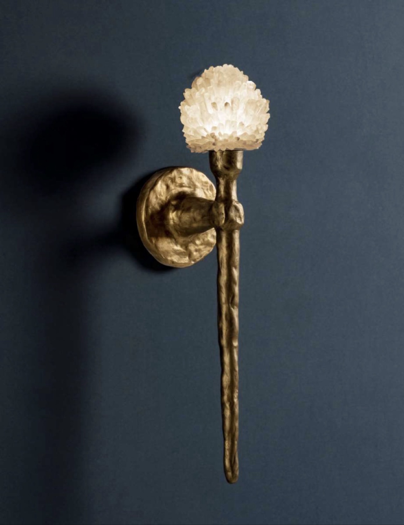 Brass wall sconce crowned with a glowing clear quartz cluster against a deep slate wall